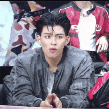 a young man in a gray jacket is making a funny face while sitting at a table .