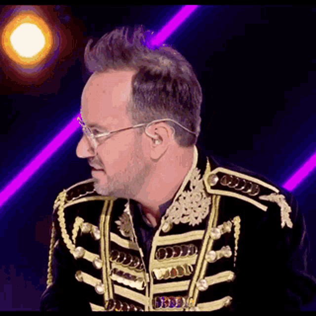 a man wearing a black and gold jacket and glasses is standing on a stage .