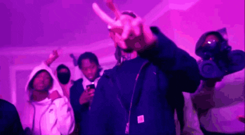 a group of people are standing in a room with purple lights and a man is making a peace sign .