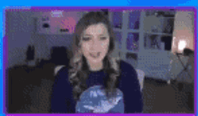 a woman in a blue sweater is sitting in front of a purple screen .