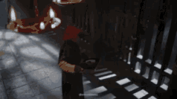 a man in a red hat is standing in a dark room with candles on the ceiling .
