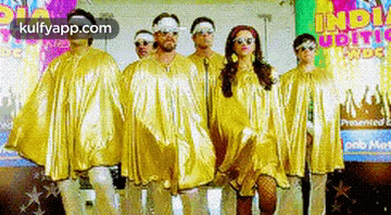 a group of people dressed in gold standing next to each other in front of a colorful sign .