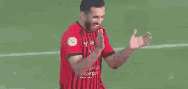 a man in a red and black striped shirt is standing on a soccer field next to another man in a yellow shirt .