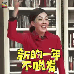 a woman in a red shirt is waving her hand in front of a bookshelf with chinese writing on it .