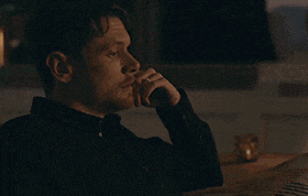 a man in a black shirt is sitting at a table with his hand on his chin