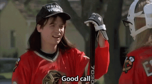 a boy in a wayne woods hat is holding a hockey stick while talking to another boy .