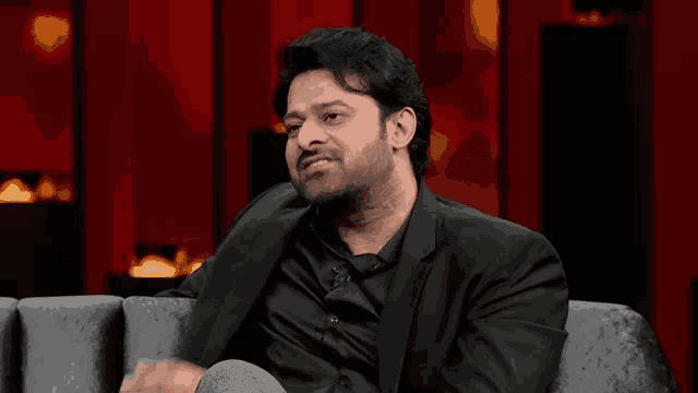 a man in a black suit is sitting on a couch with his hands outstretched