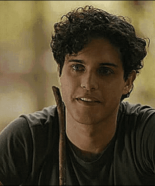 a young man with curly hair is smiling and holding a stick in his mouth .