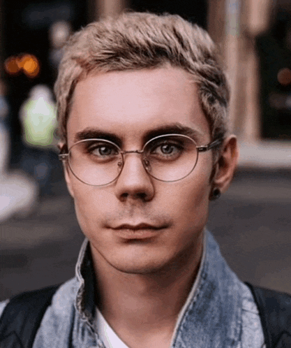 a man wearing glasses and a denim jacket is looking at the camera