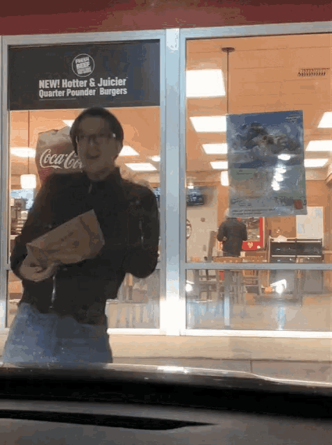 a man standing in front of a window with a sign that says hotter and juicier quarter pounder burgers