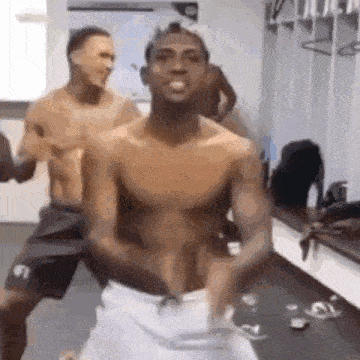 a shirtless man is standing in a locker room with a towel around his waist .