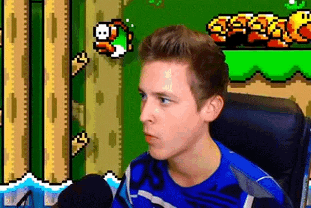 a young man in a blue shirt is sitting in front of a microphone in front of a video game screen .