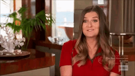 a woman in a red shirt is standing in front of a window and smiling .