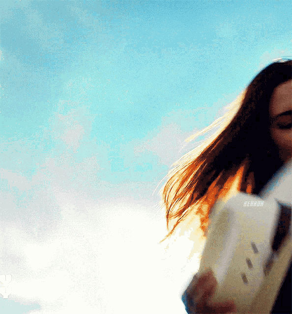 a woman with long hair is holding a book in front of a blue sky ..