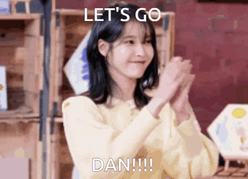 a woman in a yellow sweater applauds with the words let 's go dan !!!