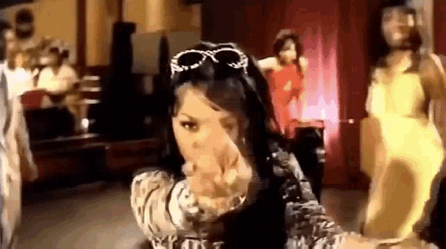 a woman wearing sunglasses is dancing in a room with a group of people .