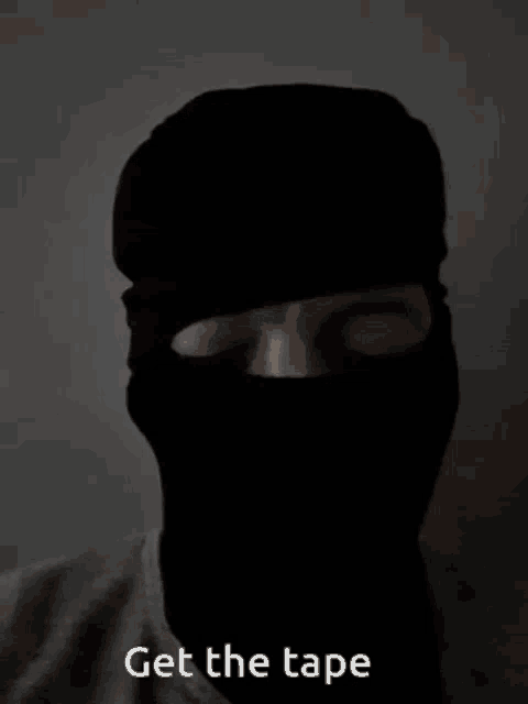 a man wearing a black balaclava with the words get the tape below him