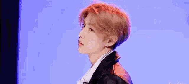 a young man with red hair is standing in front of a blue background and looking at the camera .