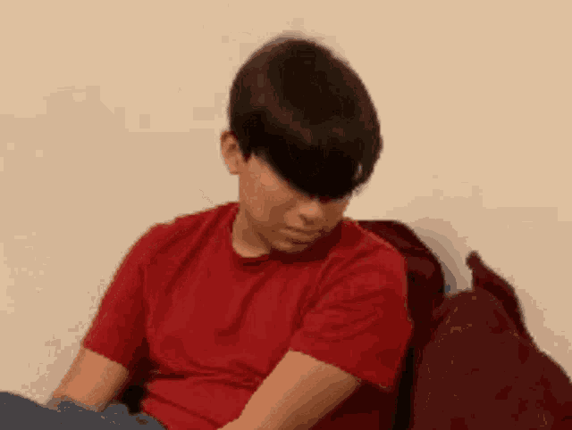 a young boy in a red shirt is sitting on a couch with his eyes closed .