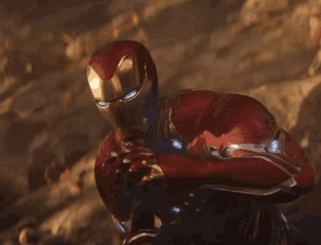 iron man is kneeling down in the dirt and holding a gun in his hand .