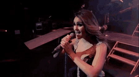a woman is singing into a microphone on a stage in front of a crowd .