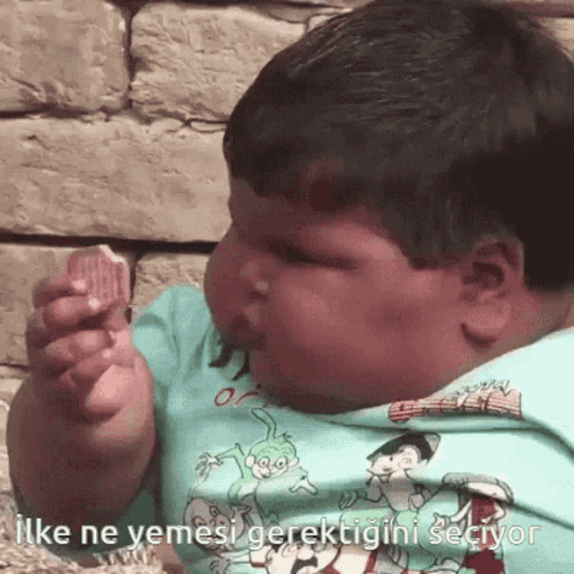 a baby in a blue shirt is eating a piece of food with the words " ilk ne yemesi gerektiğini seçiyor " on the bottom