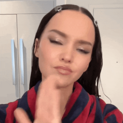 a woman wearing a red and blue striped shirt is touching her face