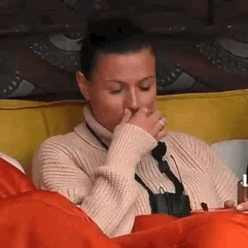 a woman in a sweater is sitting on a couch covering her mouth .