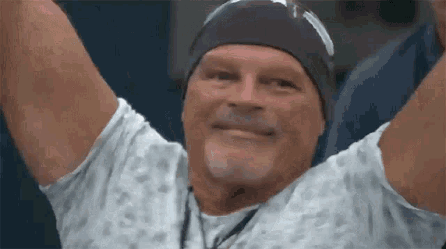 a man in a hospital gown with his arms in the air is smiling .