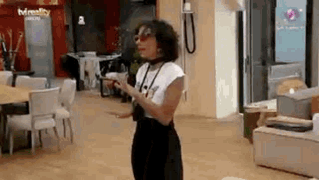 a woman is standing in a living room with her arms outstretched and looking at her phone .