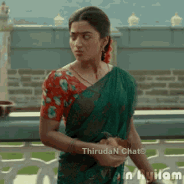 a woman in a green saree and a red blouse is standing on a balcony .
