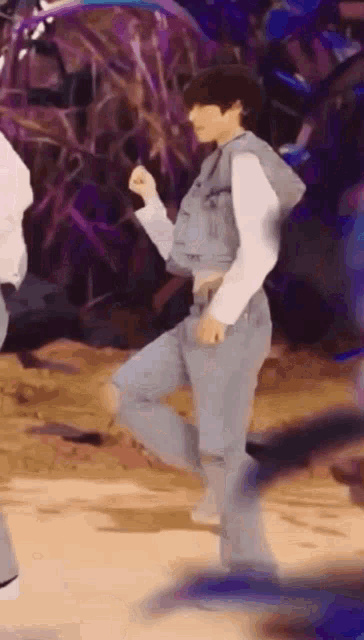 a man in a denim vest and jeans is dancing on a stage with other people .
