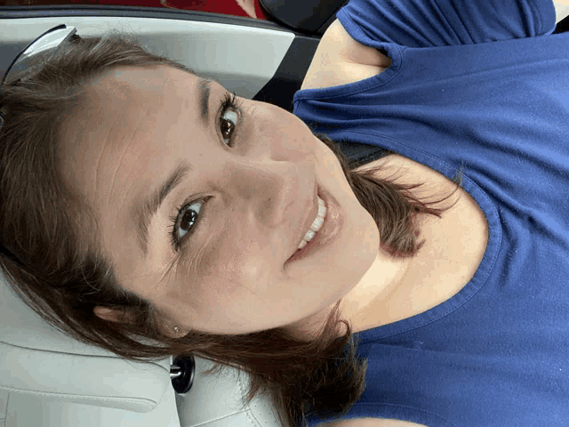 a woman in a blue shirt is smiling while laying in a car