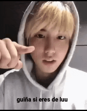 a young man wearing a white hoodie is making a heart shape with his finger .