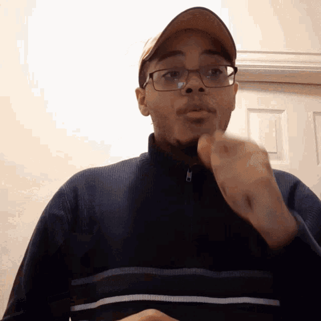 a man wearing glasses and a hat is making a gesture