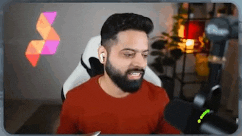 a man with a beard is sitting in a chair in front of a microphone and looking at the camera .