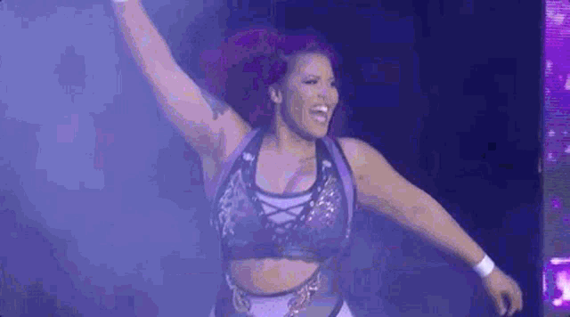 a female wrestler is standing on a stage with her arms in the air and smiling .