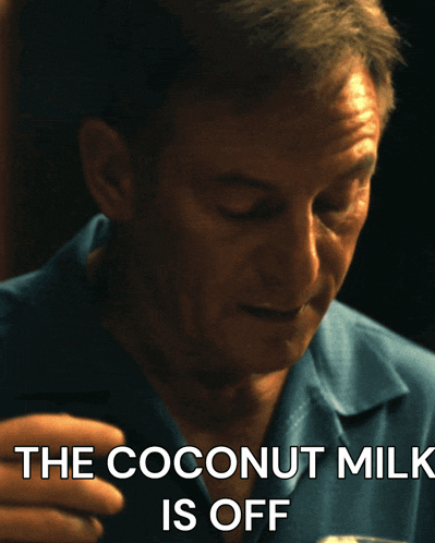 a man in a blue shirt is drinking a glass of coconut milk with the caption the coconut milk is off