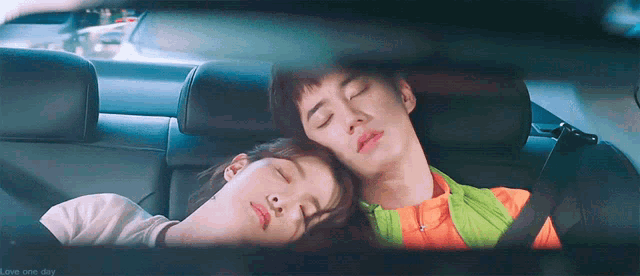 a man and a woman are laying in the back seat of a car with their eyes closed .