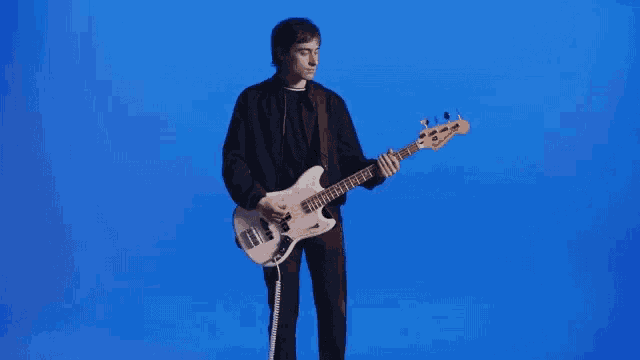 a man in a black suit is playing a white bass guitar in front of a blue background .