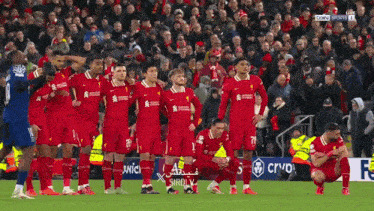 a group of soccer players are kneeling on the field with a crowd behind them