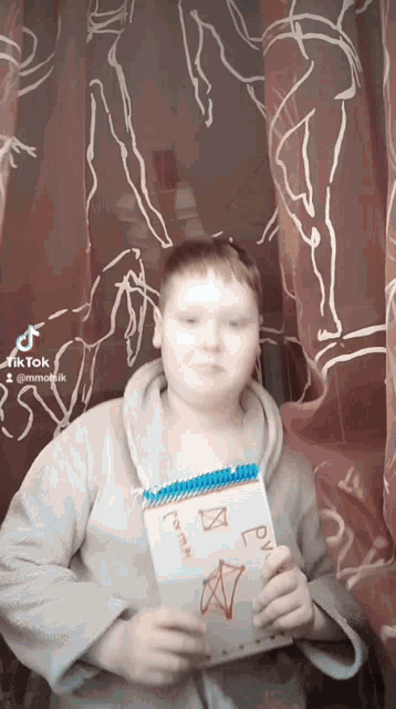a boy is holding a notebook with a drawing on it that says ' rv ' on it