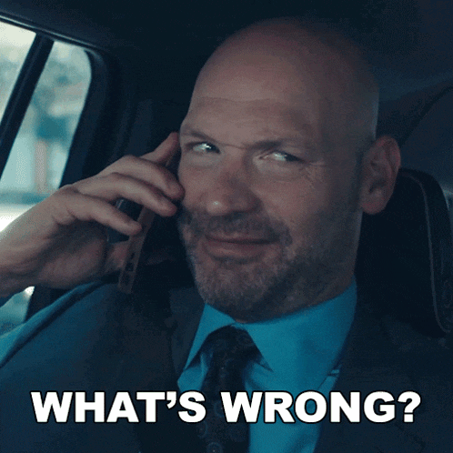 a man in a suit and tie is talking on a cell phone with the words what 's wrong behind him