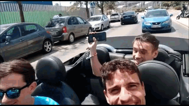 a group of men are taking a selfie in a convertible car with a blue car behind them that says ibiza