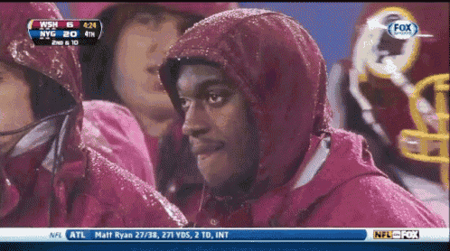 a man wearing a hooded jacket watches a football game on fox