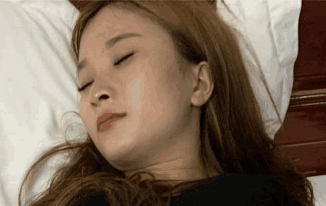 a woman is sleeping on a bed with her eyes closed and her mouth open .