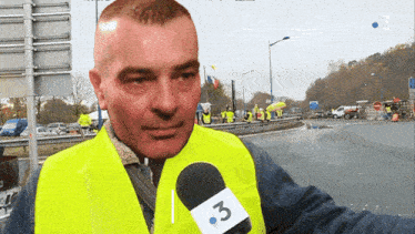 a man wearing a yellow vest is talking into a microphone that has the number 3 on it
