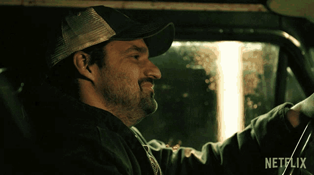 a man wearing a hat is driving a car with a netflix logo behind him