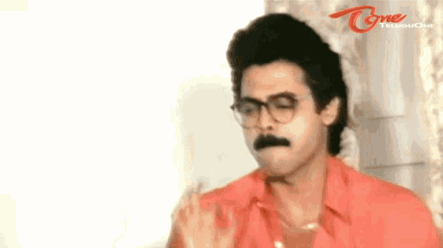 a man with glasses and a mustache is standing in front of a white wall .
