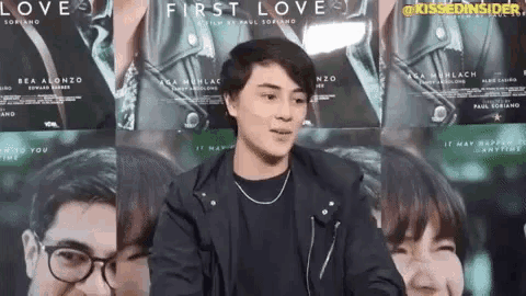 a man in a black jacket is standing in front of a wall with posters for the movie first love